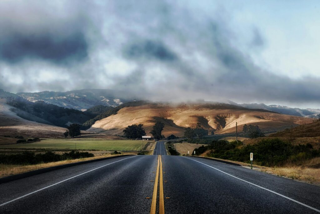 Dramatic sky over a deserted highway flanked by rolling hills, ideal for travel themes.
