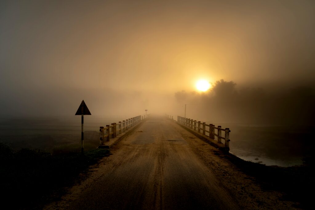 A serene sunrise scene of a foggy bridge enveloped in mist, casting a moody atmosphere.