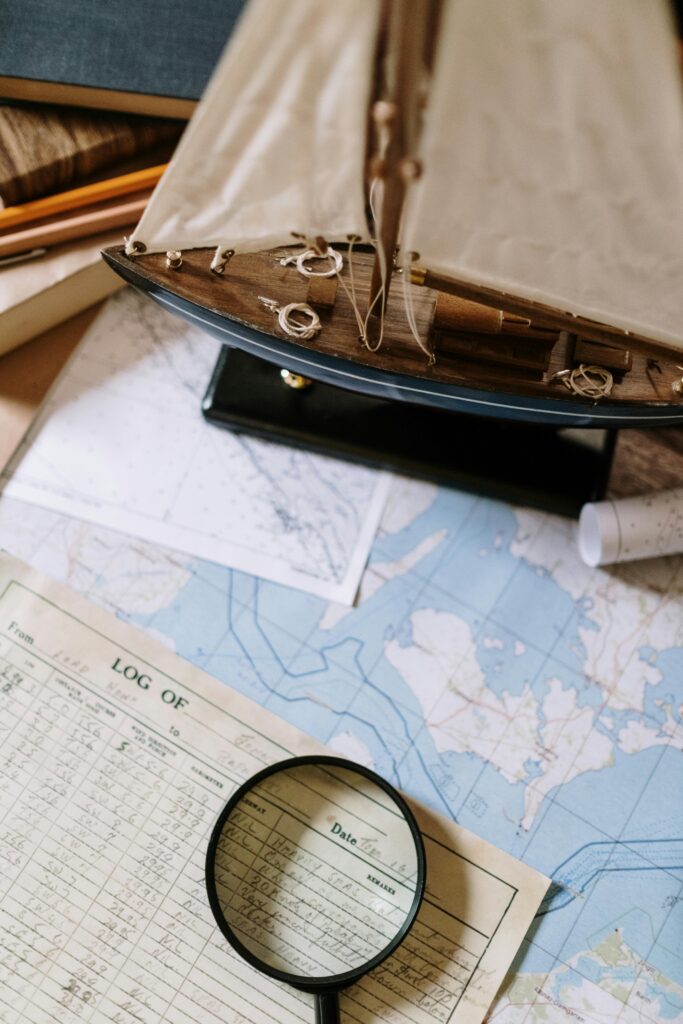 Close-up of nautical maps with a magnifying glass and model ship, ideal for maritime and exploration themes.