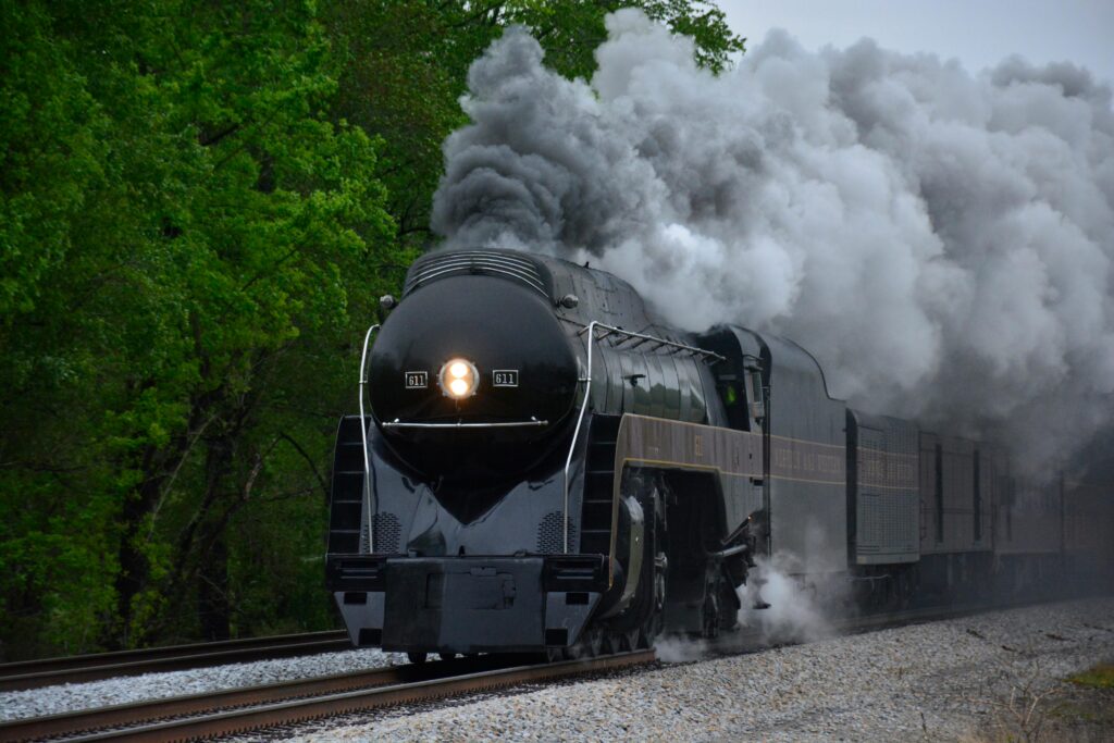Powerful steam locomotive traversing lush countryside with smoke billowing.
