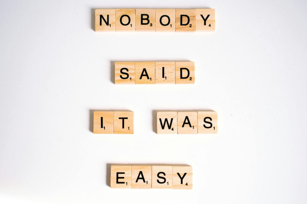 Close-up of wooden Scrabble tiles spelling 'nobody said it was easy' on a white background.