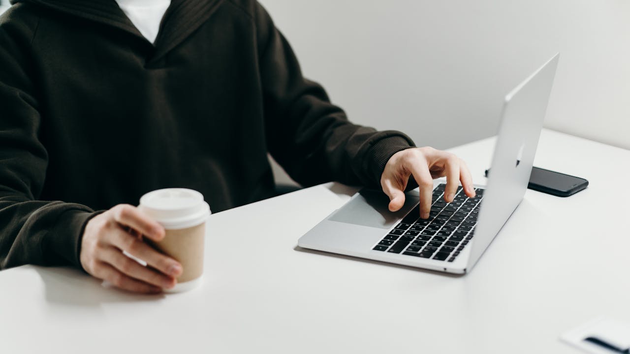 Casual home office setup with a person typing on a laptop while holding a coffee cup.