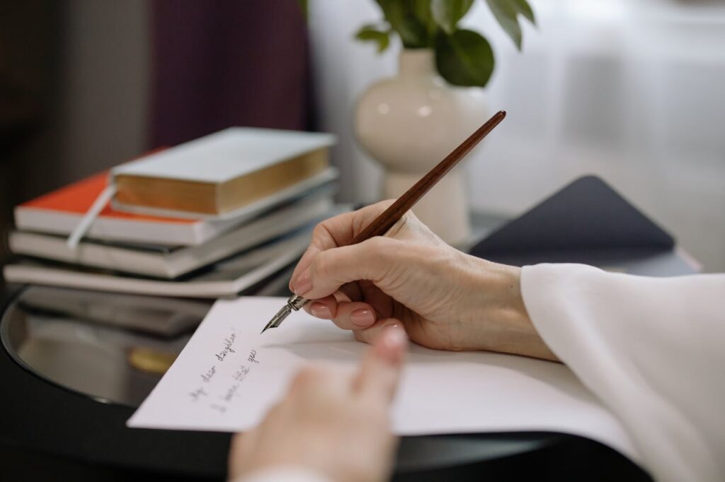 pexels photo 6918487 A close-up of a person writing with a fountain pen on paper, books stacked nearby indoors.