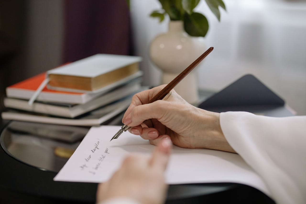 Tangot tantsitakse ikka kahekesi. Vol 1 A close-up of a person writing with a fountain pen on paper, books stacked nearby indoors.